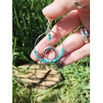 Boucle d’oreille Atlante en apatite bleue création Magic Gaïa tenue entre les doigts, anneau argenté et charms soleil, photo en extérieur sur fond d’herbe et bois, communication, clarté mentale, apaisement, confiance en soi