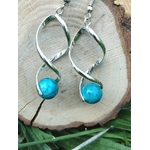 Boucles d’oreilles spirales argentées avec perles d’apatite bleue posées sur rondin de bois et décor végétal, clarté, motivation, confiance.