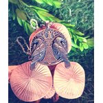 Pendentif viking en métal argenté vieilli avec arbre sacré et deux corbeaux, posé sur champignon en bois miel avec herbes vertes floues
