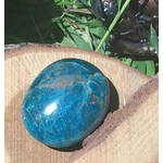 Galet d’apatite bleue polie ovale présenté dans un pochon beige avec feuillage en arrière-plan, pierre naturelle évoquant la douceur émotionnelle, la concentration et l’inspiration.