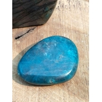 Galet d’apatite bleue poli sur support en bois avec plume noire, pierre naturelle associée à la lucidité, à l’expression posée et à l’équilibre intérieur.
