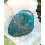 Galet d’apatite bleue poli sur fond blanc, quelques touches végétales en décor : apaisement, communication, clarté, motivation douce.