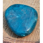 Galet d’apatite bleue polie bleu profond posé sur support naturel texturé, pierre naturelle associée à la profondeur intérieure, à l’aisance d’expression et au calme du mental.