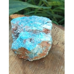 Apatite bleue brute sur support en bois avec décor végétal vert en arrière-plan, pierre naturelle associée à la lucidité, à l’élan intérieur et à l’expression sincère.