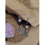 Boucles d’oreilles pendantes triquetra argenté, perles améthyste et sélénite mise en scène sur support bois/minéral – Création Magic Gaïa – invite au calme, à la clarté et à l’intuition.