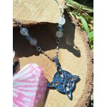 Collier nœud de sorcière bleu posé sur tranche de bois avec tissu rose et feuillage, péristérite et Aqua Aura pour apaisement et énergie protectrice