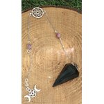 Pendule noir facetté avec chaîne argentée, perles roses et breloques triple lune, posé sur tranche de bois avec bord végétal, apporte protection, ancrage et clarté.