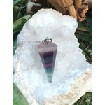 Pendule en fluorite facettée violet/vert sur chaîne argentée, posé sur amas de quartz blanc avec feuillage, aide au recentrage et à la clarté mentale.