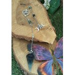 Pendule personnalisé en fluorite multicolore sur chaîne argentée avec breloques ésotériques, posé sur bois naturel avec mousse verte et papillon décoratif, apporte clarté, apaisement et intuition.