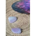 Deux pierres roulées de kunzite rose pâle aux reflets laiteux, posées sur support en bois avec une pierre sombre irisée en arrière-plan, pierres naturelles associées au réconfort, à la paix intérieure et à la sensibilité apaisée.