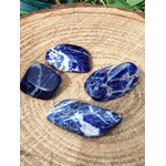 Quatre sodalites roulées bleu profond aux veines blanches sur tranche de bois clair en décor naturel, pierres naturelles liées à l’ordre des pensées, à la justesse d’expression et à la stabilité intérieure.