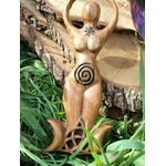 Statuette Gaïa déesse en bois avec spirale, posée dans un décor végétal (mousse/plantes) contre une écorce, ambiance nature; inspire ancrage, apaisement, protection douce, intuition et harmonie.