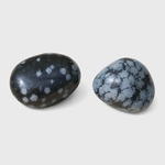 Deux pierres roulées d’obsidienne neige noir profond moucheté blanc et noir-gris marbré sur fond blanc, pierres naturelles reliées au recentrage, à la protection et à l’équilibre émotionnel.