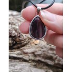 Pendentif agate du Botswana à fines bandes brun-gris sur cordon noir, tenu entre les doigts sur fond de roches, stabilité douce et présence intérieure