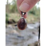 Pendentif agate du Botswana goutte tenu entre les doigts en extérieur sur pierres en Bretagne, bandes brun-gris et énergie de réconfort