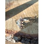 Bague réglable acier inoxydable argenté, nœud de sorcière ajouré, posée sur bois brut avec ombre marquée; symbole de protection.