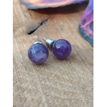 Boucles d’oreilles puces améthyste violettes en inox 304 sur planche en bois, mise au point sur les perles, fond doux et flouté; associée à sérénité, équilibre émotionnel, intuition.