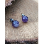 Boucles d’oreilles puces améthyste en duo sur bois brut, reflets sur les perles, arrière-plan neutre; évoque apaisement, harmonie, lâcher-prise.