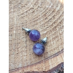 Boucles d’oreilles puces améthyste en inox 304 posées sur bois brut, deux perles violettes avec reflets, lumière naturelle; évoque calme, recentrage, clarté.