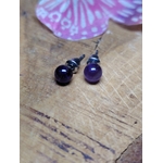Boucles d’oreilles puces améthyste sur planche en bois, duo de perles violettes en premier plan, papillon rose en arrière-plan légèrement flouté; associée à sérénité, douceur, intuition.