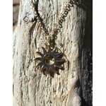 Pendentif soleil doré en acier inoxydable sur chaîne fine, photographié sur bois patiné en Bretagne, style lumineux et présence chaleureuse