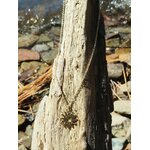 Pendentif soleil doré en acier inoxydable sur bois clair patiné et galets en Bretagne, motif ajouré rayonnant pour éclat, vitalité et confiance lumineuse