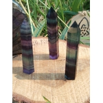 Pointe de fluorite multicolore aux nuances vertes et violettes, posée sur support en bois avec herbes en arrière-plan, pierre naturelle associée à la lucidité, au recul et à l’harmonie intérieure.