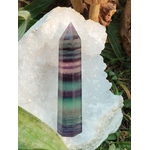 Pointe de fluorite multicolore à bandes vertes, violettes et rosées, présentée sur plaque de sélénite avec feuillage, pierre naturelle évoquant le recentrage, la douceur émotionnelle et l’alignement intérieur.