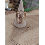 Bague Triskell dorée réglable en acier inoxydable sur porte-bague conique blanc, posée sur planche en bois; symbole cycles, équilibre, protection.