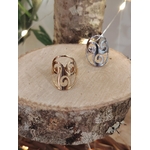 Bague Triskell dorée et bague Triskell argentée posées sur rondin de bois, feuillage en fond; symbole cycles et équilibre.