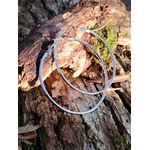Grandes créoles argentées en acier inoxydable, anneaux fins et légers, photographiées en Bretagne sur écorce de bois et feuilles sèches; évoquent élégance naturelle et légèreté.