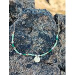 Collier doré à cristaux verts sur rochers sombres en bord de mer en Bretagne, équilibre visuel et allure naturelle raffinée