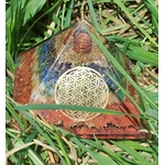 Pyramide orgonite 7 chakras avec fleur de vie et spirale de cuivre, posée dans l’herbe (photo nature) ; évoque harmonie, équilibre, protection.