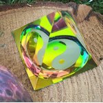 Pyramide décorative en cristal irisé vert-jaune avec symbole yin et yang, posée sur un support en bois texturé ; favorise l’harmonisation des polarités, l’apaisement et une atmosphère zen.