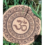 Dessous de plat rond en liège gravé symbole Om au centre, entouré d’un mandala et motifs géométriques; photo en extérieur dans l’herbe.
