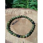 Bracelet péridot vert olive sur tranche de bois avec herbe en fond, perles naturelles pour apaisement du mental, renouveau et stabilité du ressenti