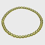 Bracelet en péridot (perles 4 mm vert olive translucide), monté sur fil élastique, présenté seul sur fond blanc en forme ovale ; rendu lumineux et naturel, évoque fraîcheur, vitalité et énergie positive.