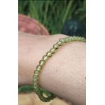 Bracelet en péridot (perles 4 mm vert olive translucide), monté sur fil, porté au poignet ; photo en extérieur avec feuillage vert en arrière-plan, ambiance fraîche et lumineuse, évoque vitalité, optimisme et légèreté.