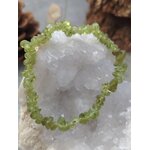 Bracelet péridot baroque (chips vert olive translucides) formant un cercle autour d’une géode blanche, posé sur un décor naturel (mousse/bois) avec arrière-plan doux, photo en gros plan.