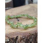 Bracelet péridot baroque sur tranche de bois avec écorce visible, gros plan sur chips verts translucides pour confiance intérieure et respiration émotionnelle
