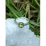 Bague péridot facetté réglable en cuivre blanc, posée sur une géode blanche, herbes vertes en arrière-plan ; apporte apaisement et clarté