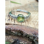 Bague péridot facetté vert olive, monture réglable, posée sur tronc texturé ; soutient la sérénité, la confiance et l’harmonie intérieure.