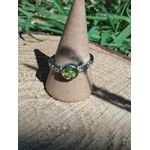 Bague réglable en cuivre blanc, péridot facetté lumineux, mise en scène sur support beige et bois ; encourage confiance et énergie positive.