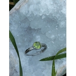 Bague réglable en cuivre blanc avec péridot facetté, posée sur une géode blanche cristallisée ; aide à retrouver optimisme, clarté mentale et élan positif