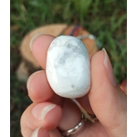 Pierre roulée howlite blanche veinée de gris tenue entre les doigts, décor végétal flouté en arrière-plan, pierre naturelle évoquant la douceur émotionnelle, la communication apaisée et le recentrage.