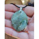 Pendentif en garniérite verte sur cordon noir, tenu en main avec pierre polie facettée et bélière argentée, pierre naturelle associée à la lucidité, à l’apaisement et à la confiance intérieure.