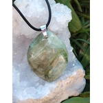Pendentif en garniérite vert pâle sur cordon noir avec bélière argentée, posé sur géode blanche et herbes vertes, pierre naturelle associée à la douceur, au recentrage et à l’équilibre intérieur.