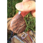 Pendentif goutte en pierre de lune noire polie tenu entre les doigts, avec herbe et feuillage en arrière-plan, bijou en pierre naturelle évoquant la sensibilité maîtrisée, l’équilibre du cœur et la présence à soi.