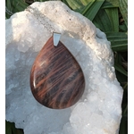 Pendentif goutte en pierre de lune noire polie sur chaîne argentée, posé sur une géode blanche avec feuillage en arrière-plan, bijou en pierre naturelle lié à l’apaisement, à l’intuition calme et à la stabilité intérieure.