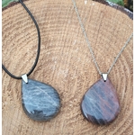 Deux pendentifs goutte en pierre de lune noire polie, l’un sur cordon noir et l’autre sur chaîne argentée, posés sur une tranche de bois, bijoux en pierre naturelle associés à la paix intérieure, à l’ancrage et à l’harmonie émotionnelle.